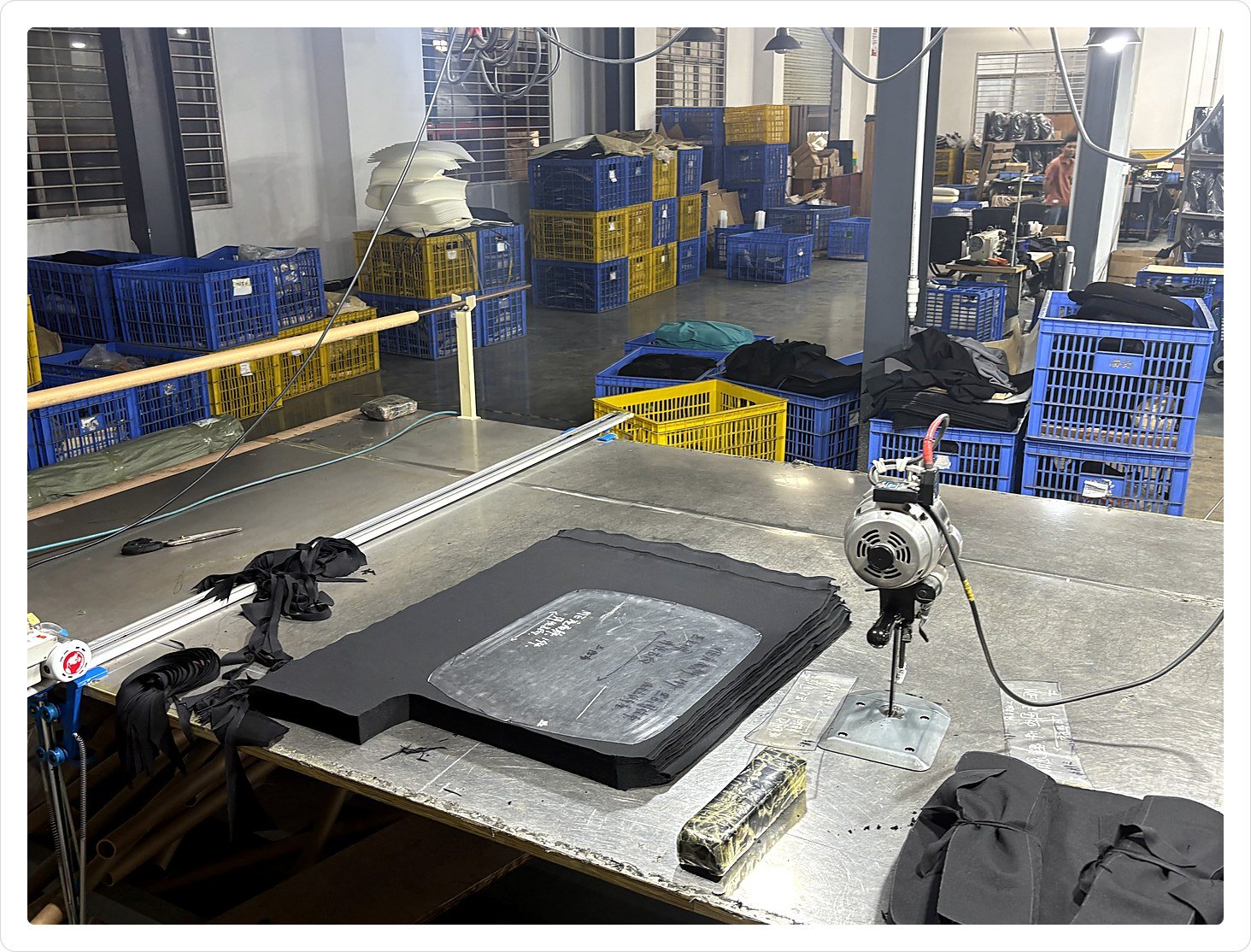 Fabric cutting table with stacked black office chair panels beside a vertical electric cutting machine