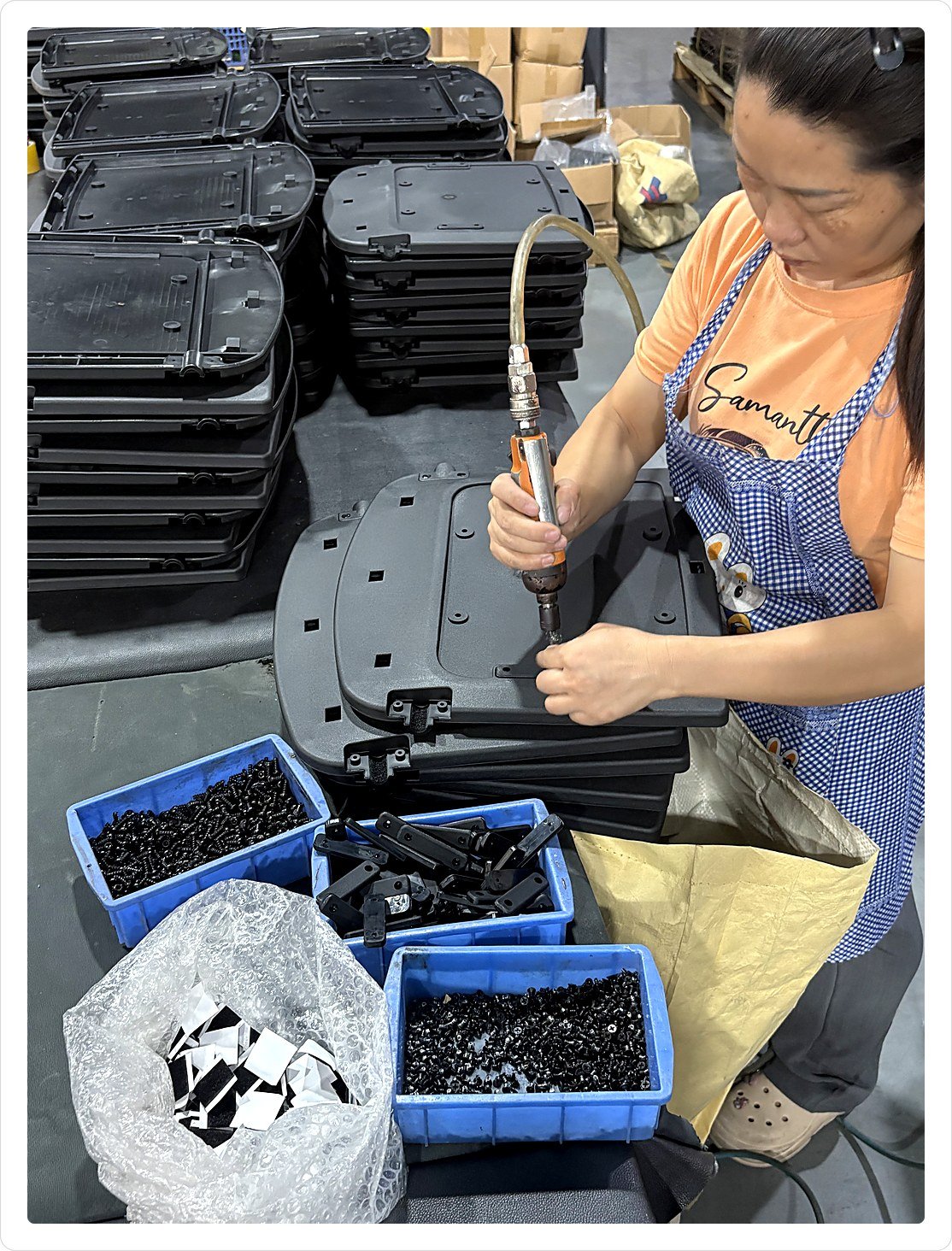 Operator driving fixings into stacked office chair seat frames with a pneumatic tool at the assembly bench