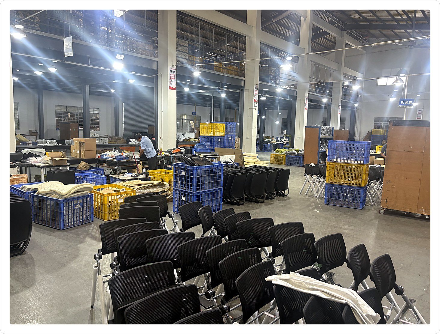 Office chair assembly hall at Via Furniture, with mesh chair backs staged on frames between colour-coded crates